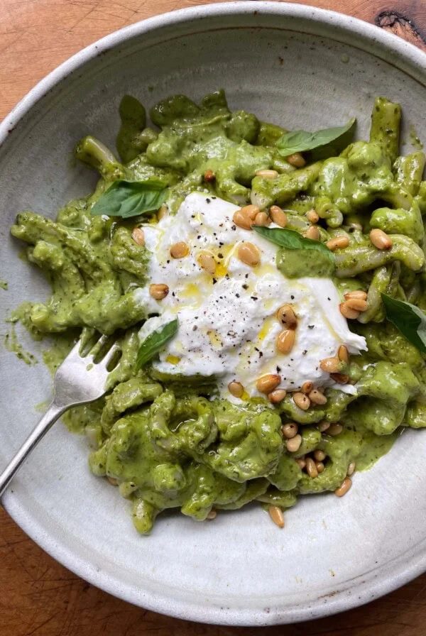 Stone bowl of pesto pasta with burrata and toasted pine nuts.