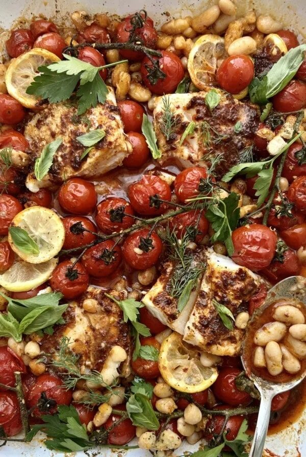 Close up of a traybake of harissa cod, cherry tomatoes, lemons and white beans.