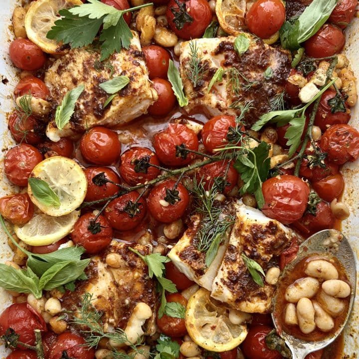 Close up of a traybake of harissa cod, cherry tomatoes, lemons and white beans.