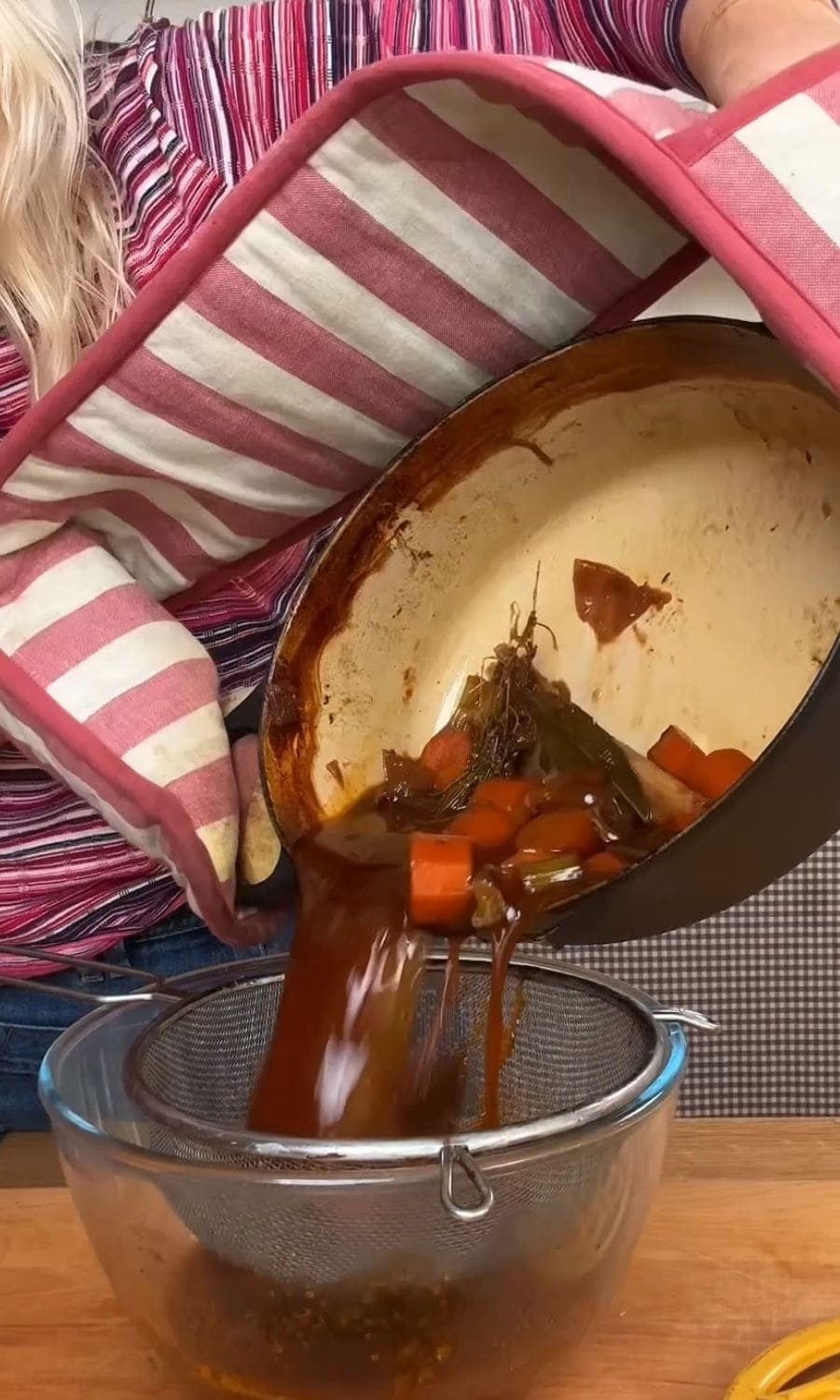 Straining braised short rib sauce to remove vegetables and herbs.