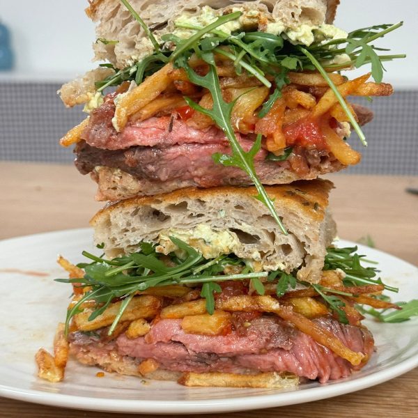 A stack of rib eye steak sandwich with chips, bearnaise butter and rocket