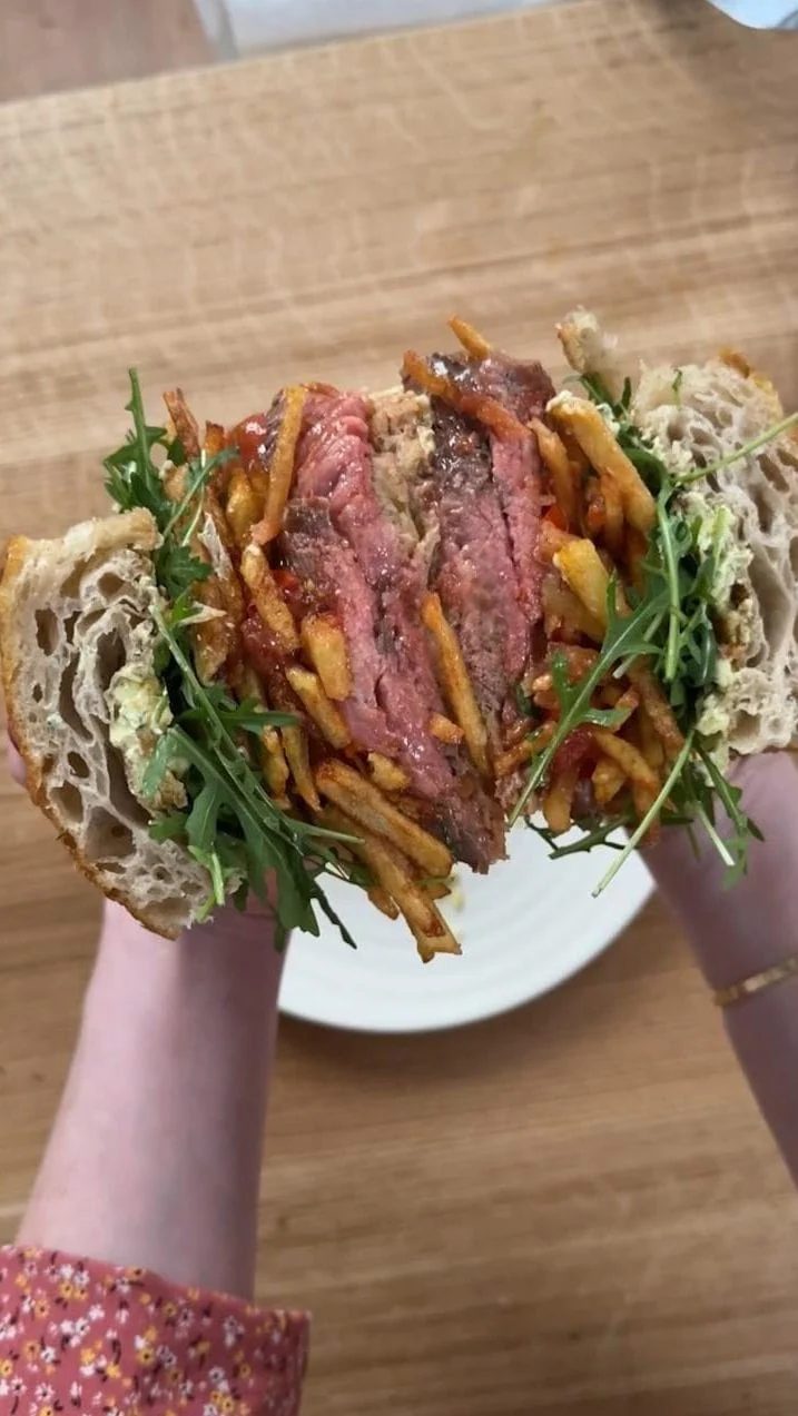 Woman holding a rib eye steak sandwich with chips, tomatoes, rocket, bearnaise butter