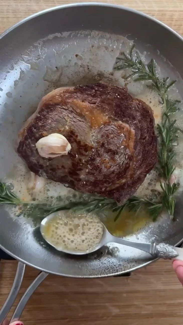 Woman basting the rib eye steak in rosemary garlic butter