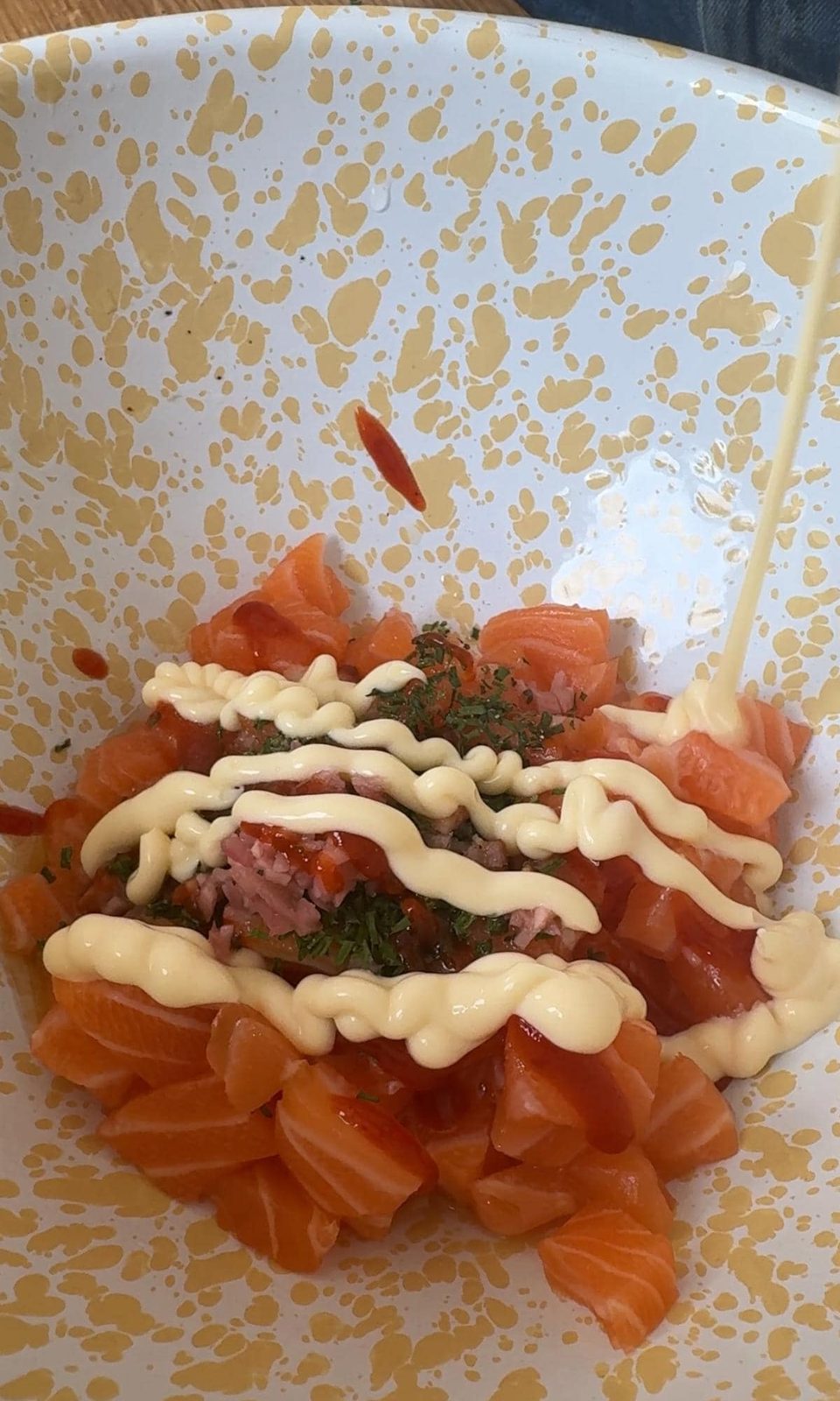 Mixing cubed salmon with dressing and seasoning ingredients in a bowl.