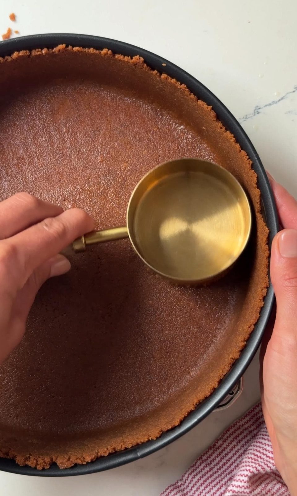 pushing the lotus biscuit base into the cheesecake tin.