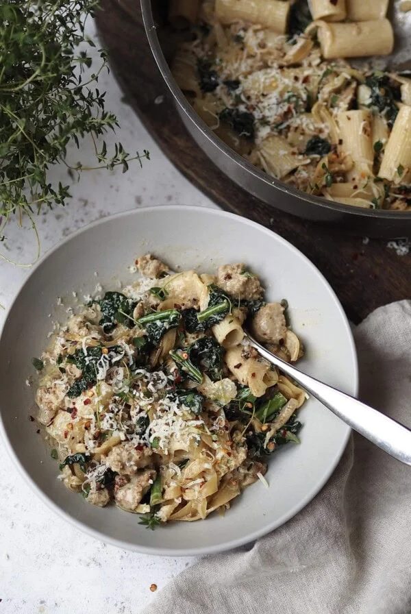 Bowl of sausage and cavelo nero pasta next to the pan and a thyme plant.