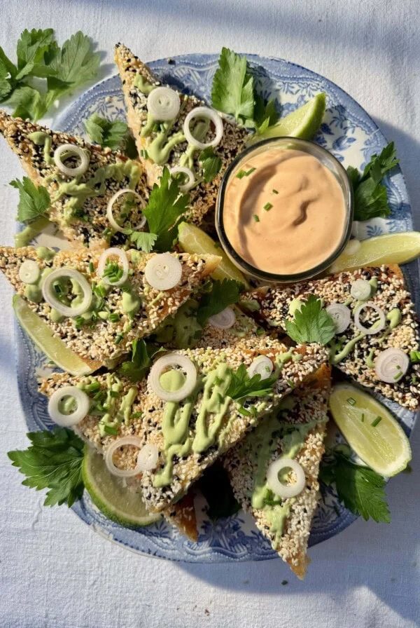 sesame prawn toasts with limes and green sauce drizzled on top.