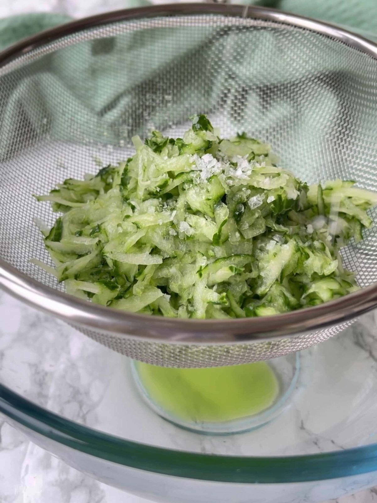 Draining shredded cucumber in sieve.