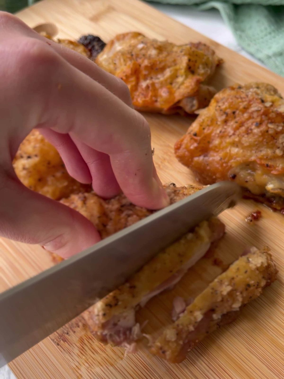 Slicing cooked chicken with knife on cutting board.