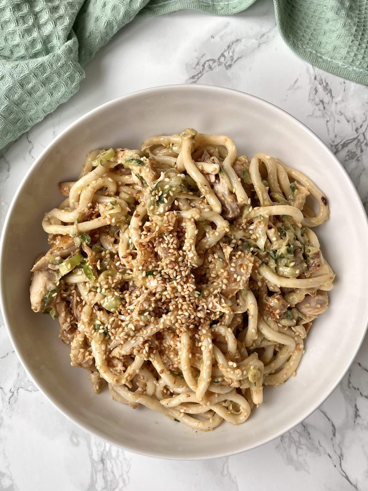 White bowl with chicken and udon noodle salad topped with sesame seeds.