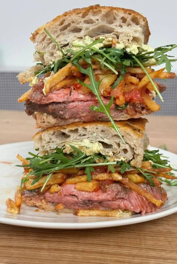 A stack of rib eye steak sandwich with chips, bearnaise butter and rocket