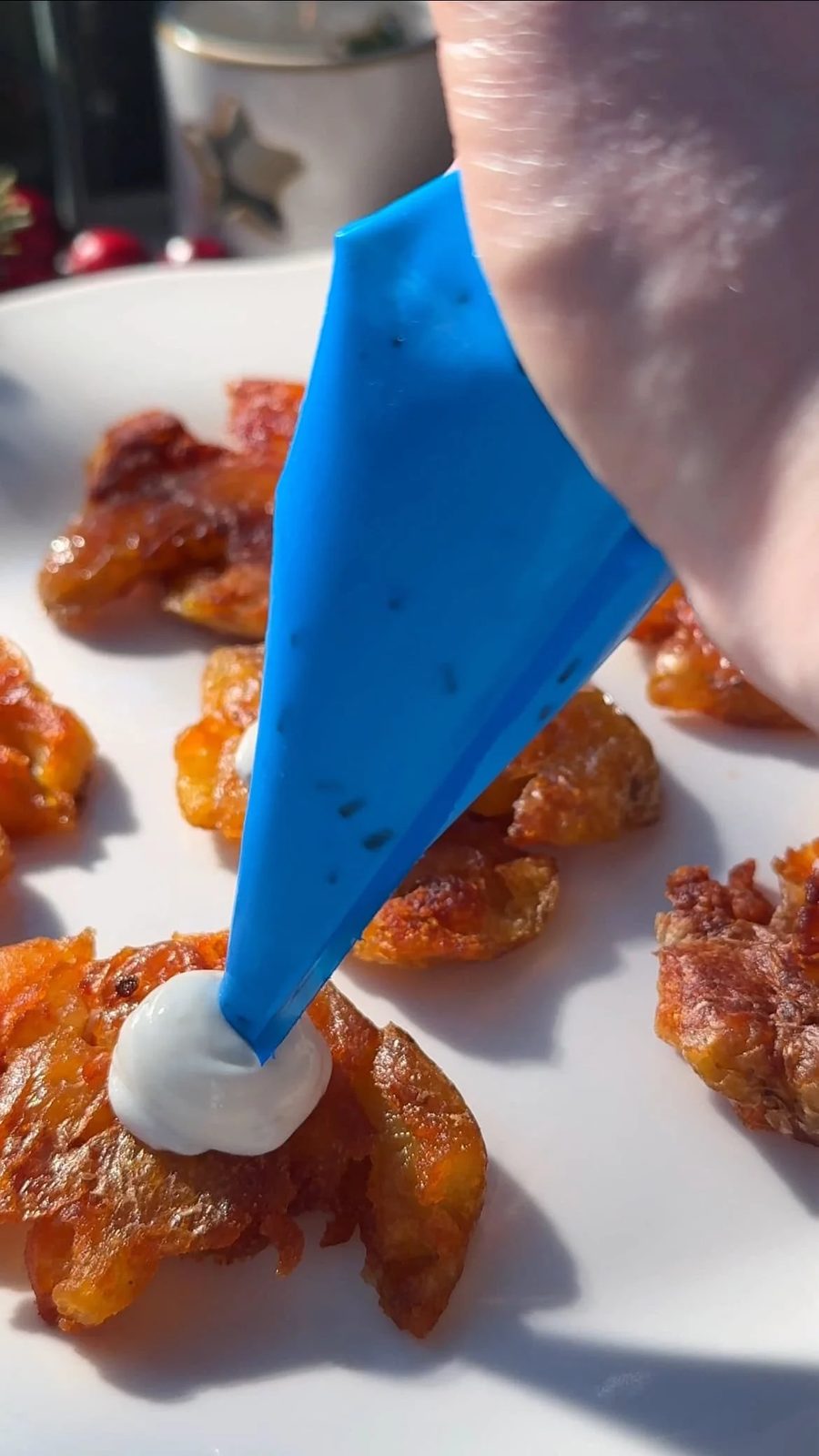 Piping creme fraiche over fried smashed potatoes.
