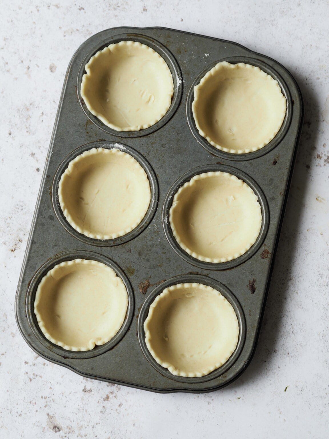Muffin tin lined with shortcrust pastry.