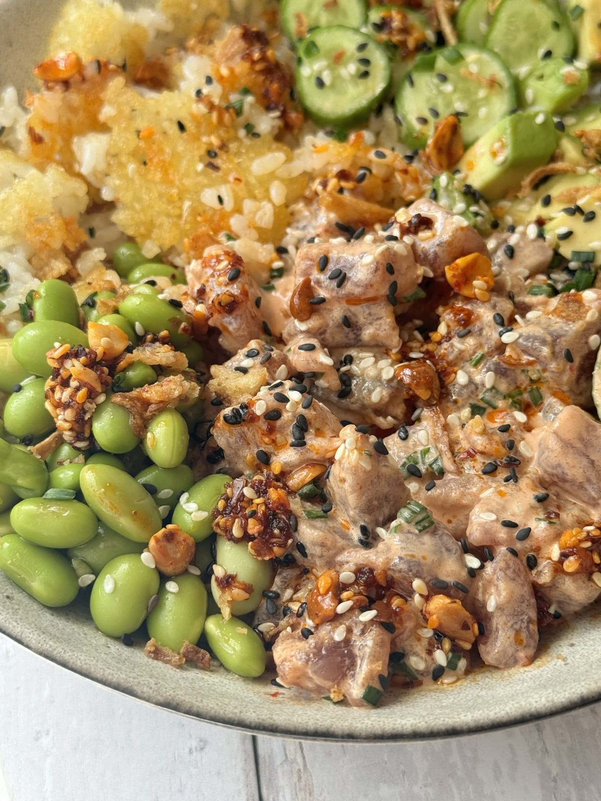 Spicy tuna in a bowl with crispy rice and cucumber and avocado in bowl.