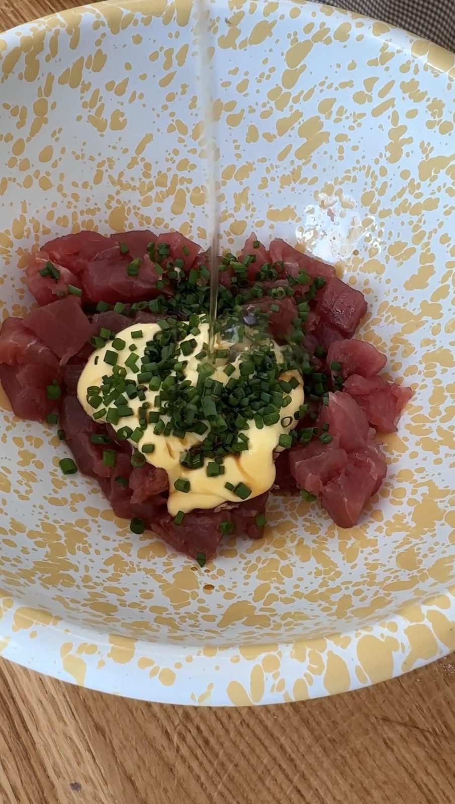 Pouring oil over tuna, mayo, and herbs in small bowl.