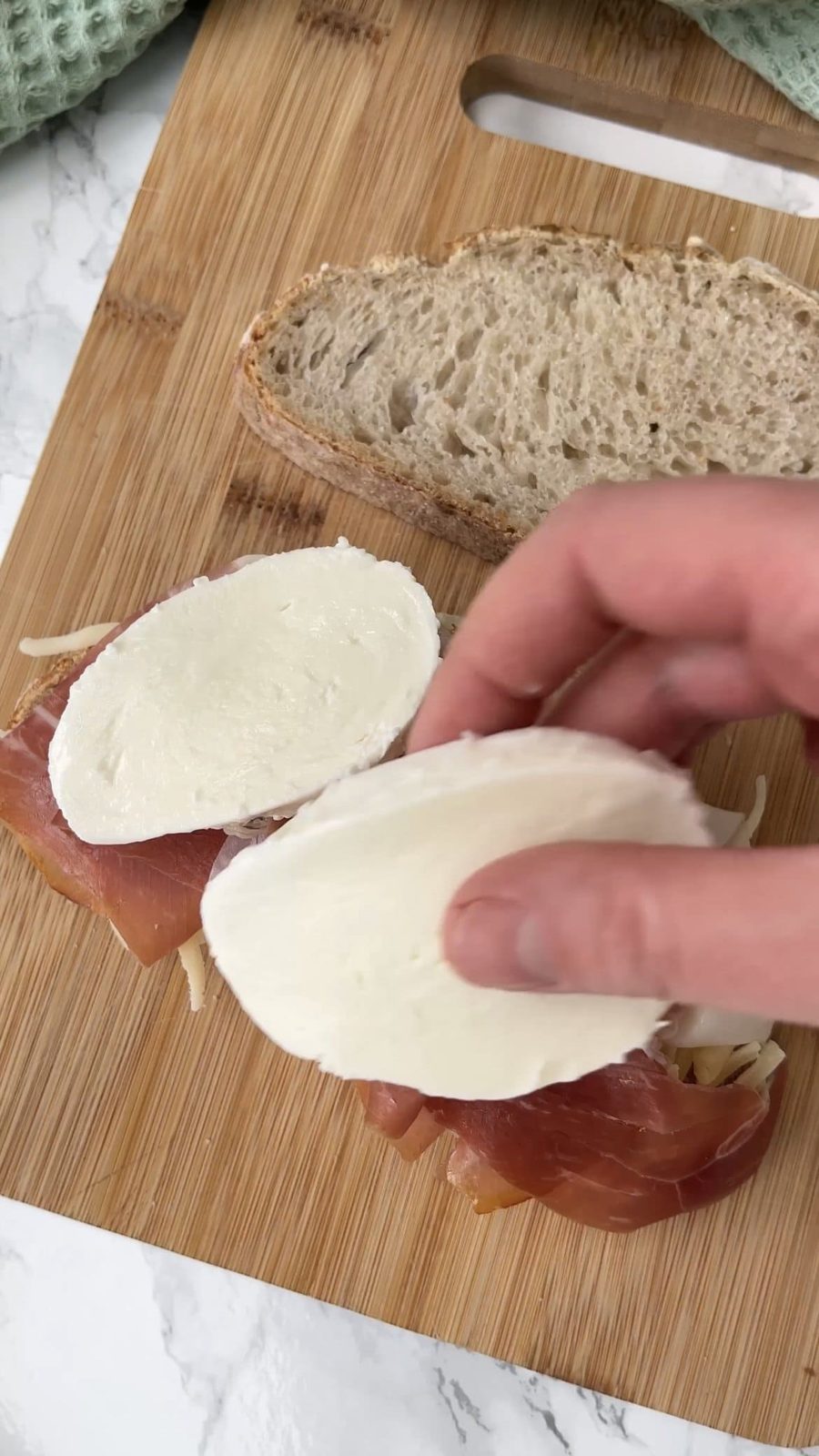 Layering grated cheese, prosciutto, and mozzarella on bread.