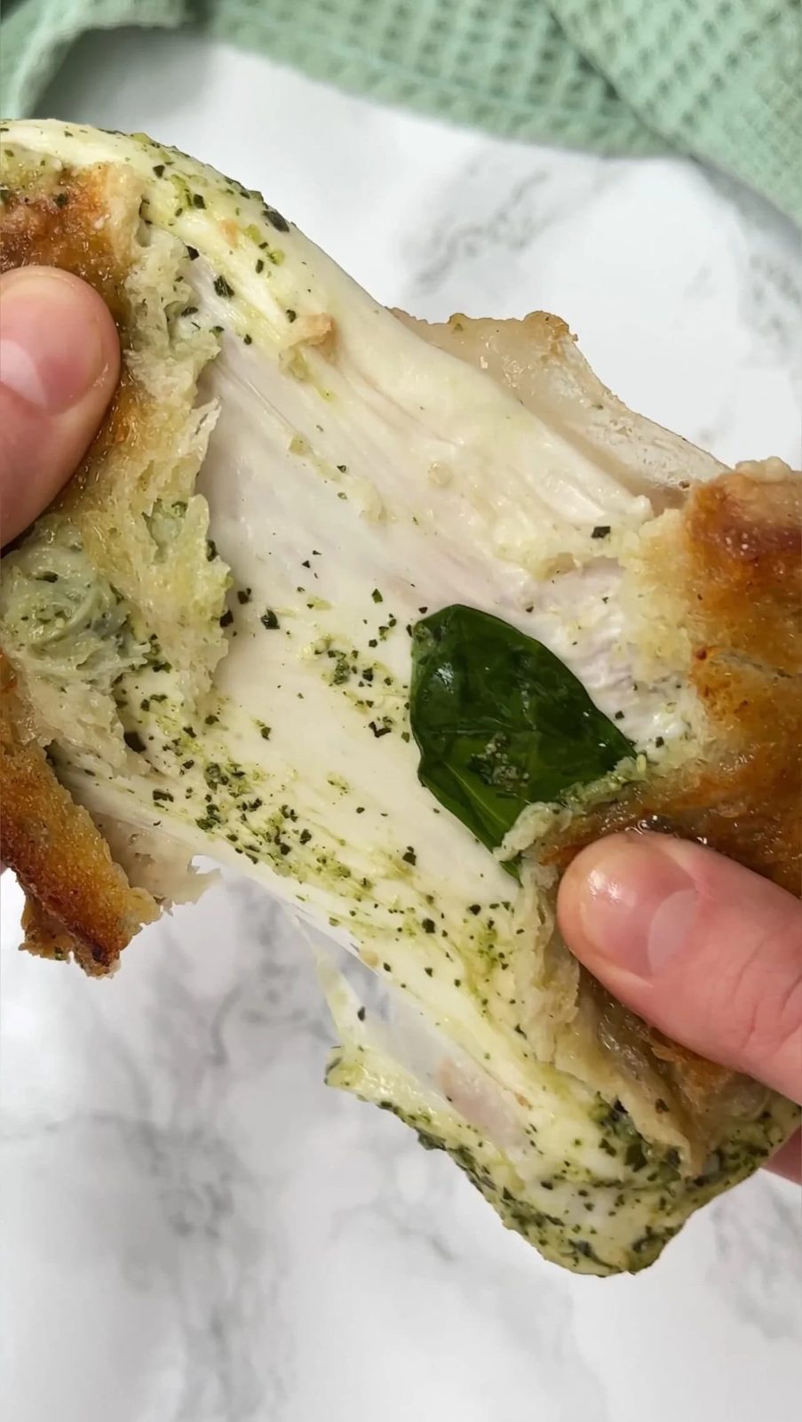 Pulling apart cheesy sandwich with basil and pesto.