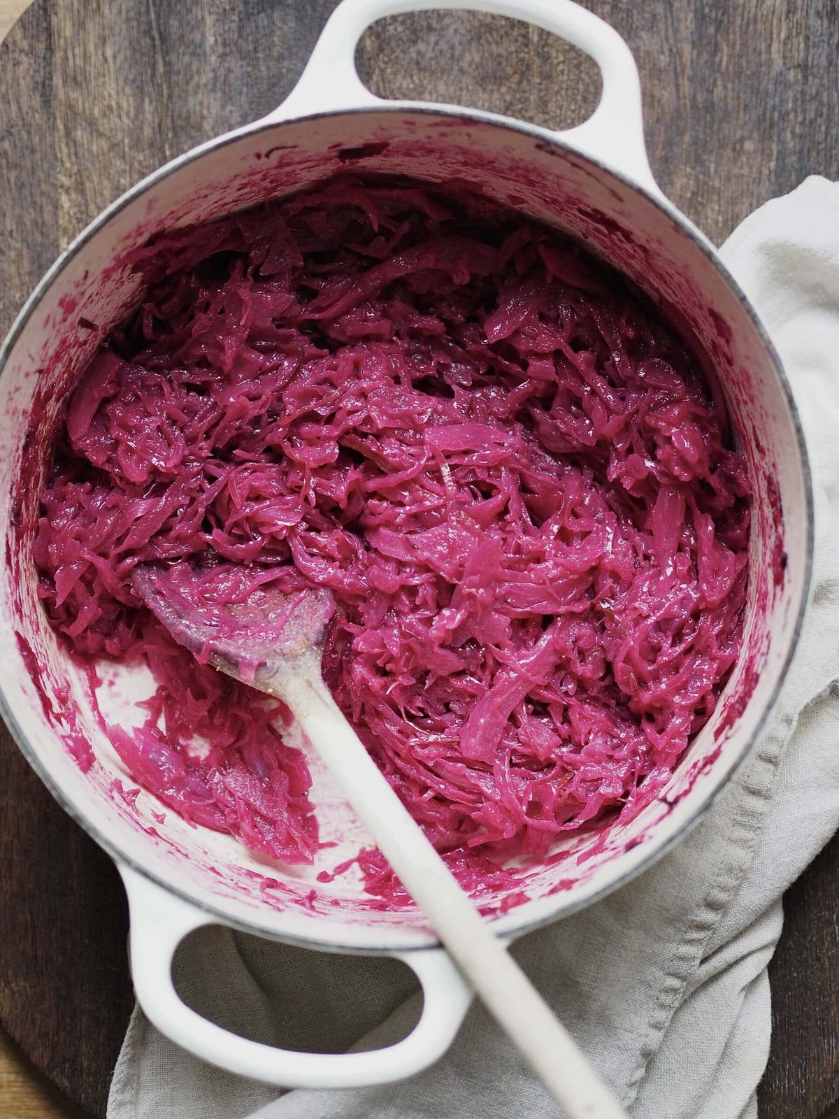 Cooked red cabbage being stirred with a wooden spoon in a white casserole dish.