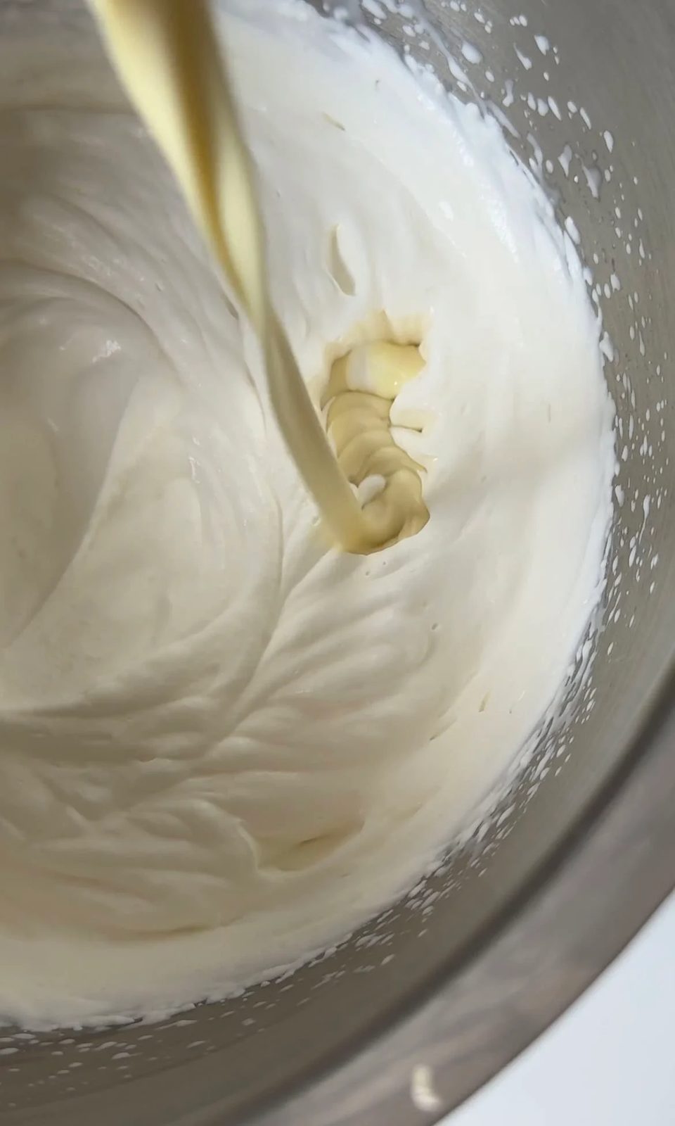 pouring melted white chocolate into whipped cream.