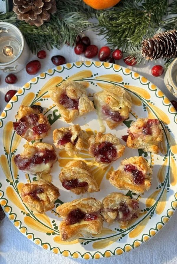 Brie puff pastry bites with cranberry sauce arranged on plate.