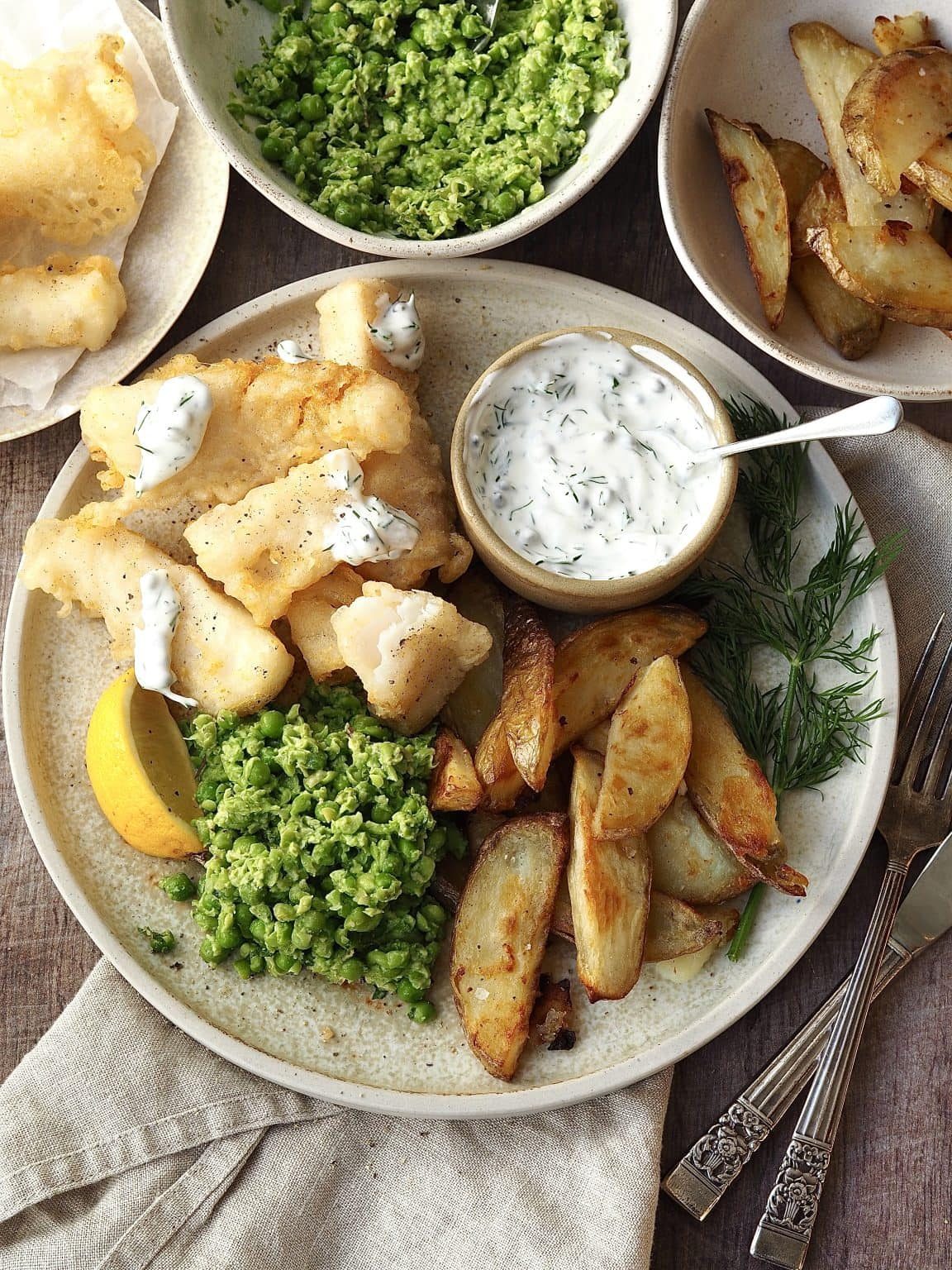 Plate of tempura cod and chips with homemade smashed minty peas and tartare sauce.
