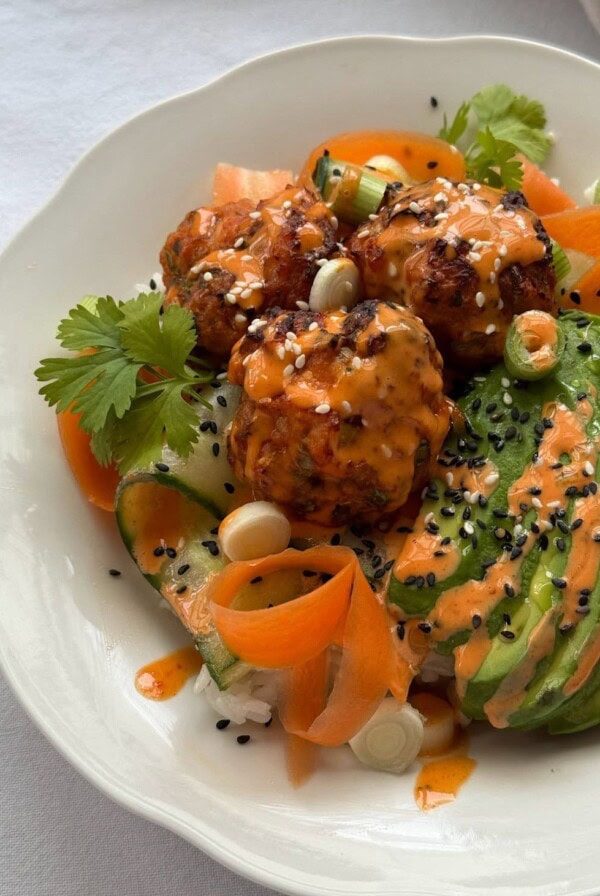 Close up of Korean flavoured salmon fishcakes served over rice with sliced avocado and a gochujang mayo drizzle.