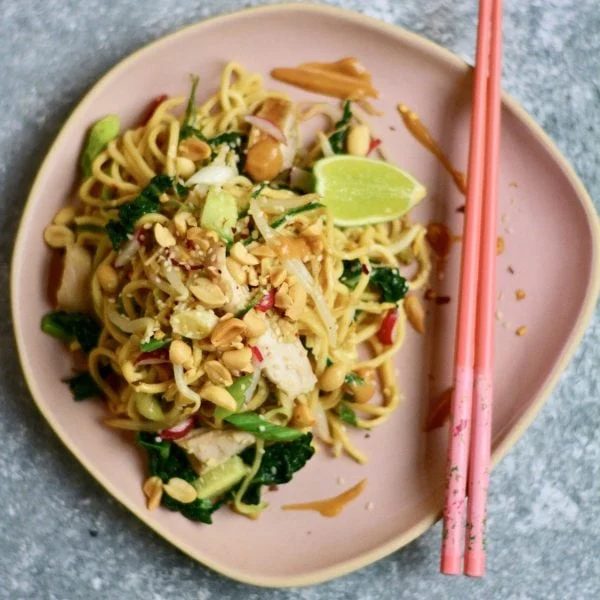 Thai-inspired noodles with chicken on plate with chopsticks.