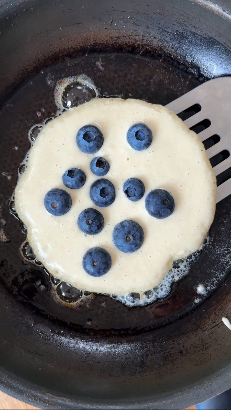 Fresh blueberries on pancake frying in pan.