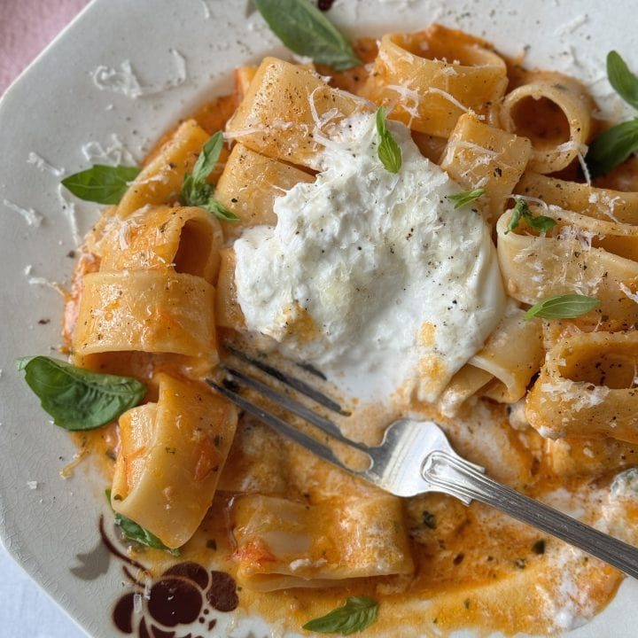 a white bowl with a fork filled with tomato butter pasta and topped with burrata.