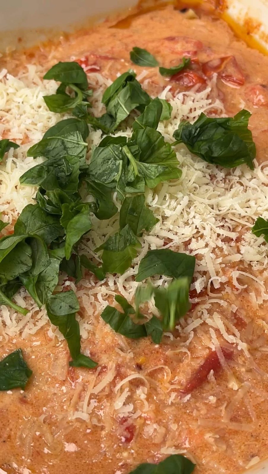 adding parmesan and basil to the tomato sauce.