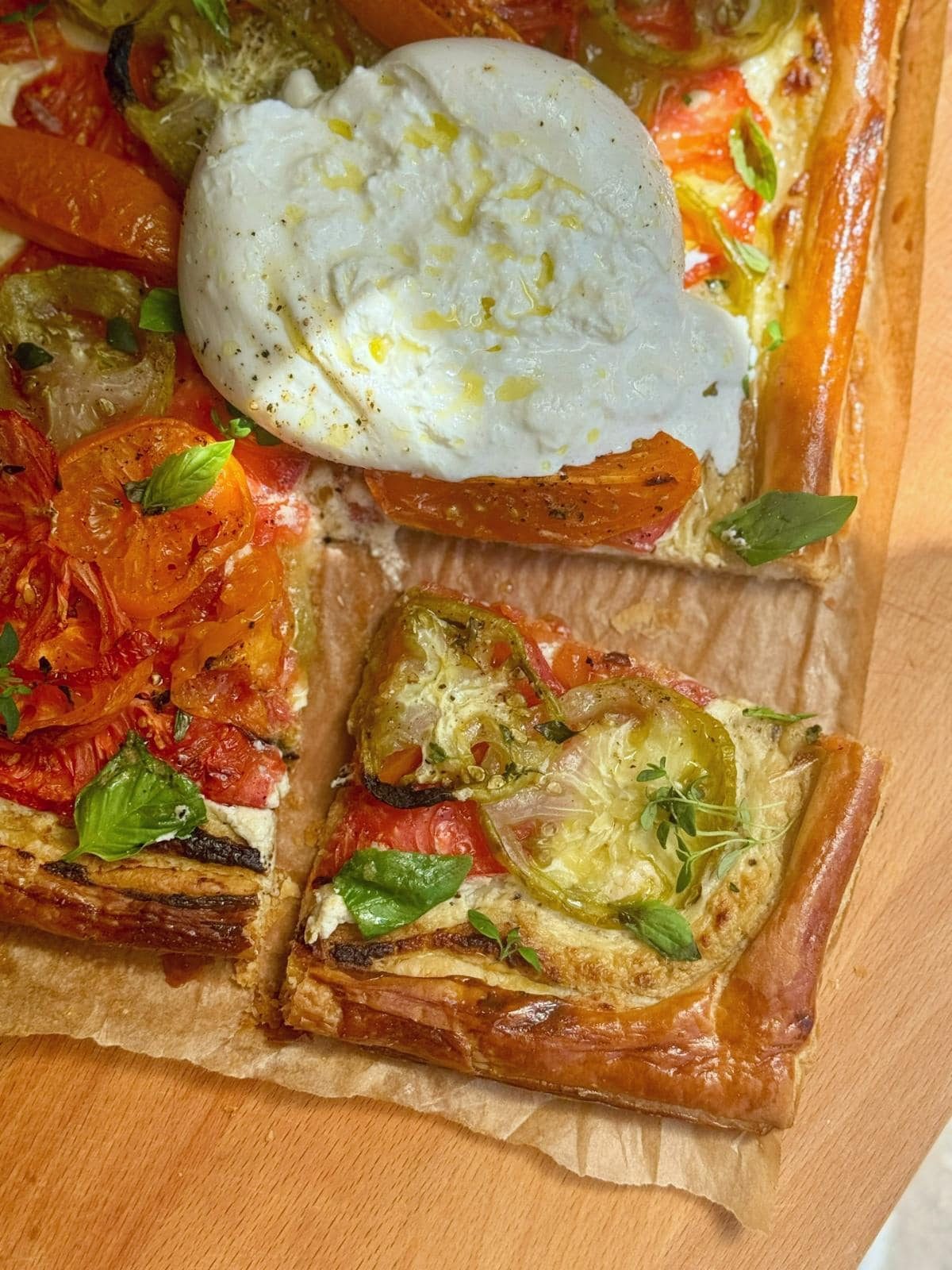 Whole and sliced tomato puff pastry tart with burrata on parchment paper.