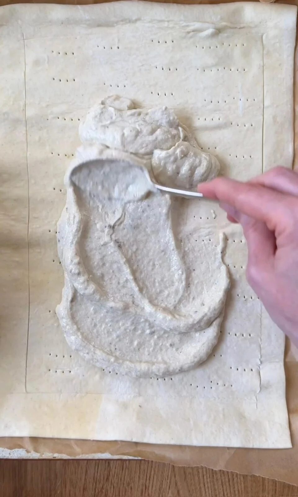 Spreading anchovy crème fraîche over raw puff pastry.