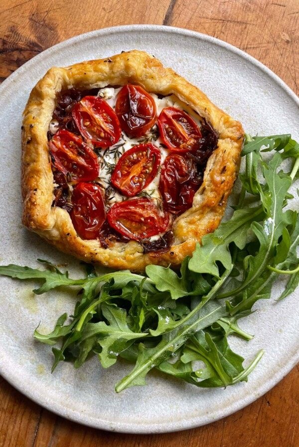 Cherry tomato, goats cheese and red onion galette on a white plate with a tangle of rocket.