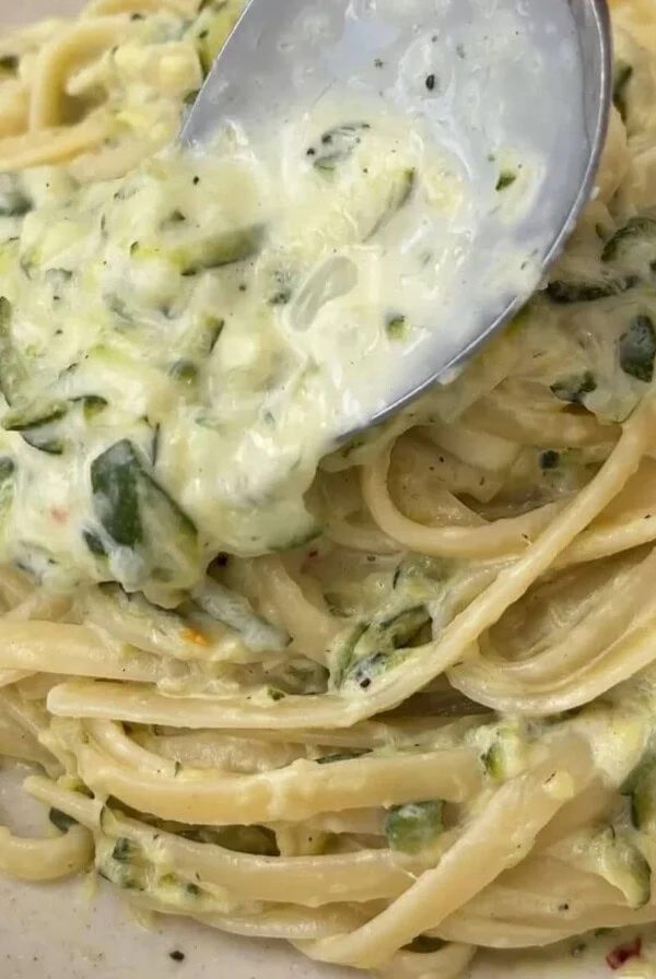 spooning sauce over courgette pasta in a beige bowl.