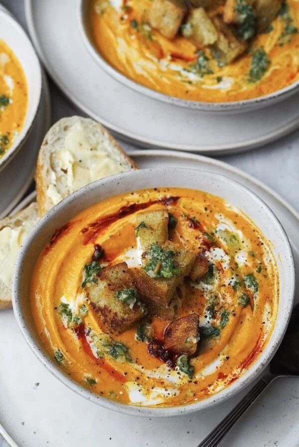 Bowl of carrot soup swirled with cream, harissa, and topped with pesto and croutons.