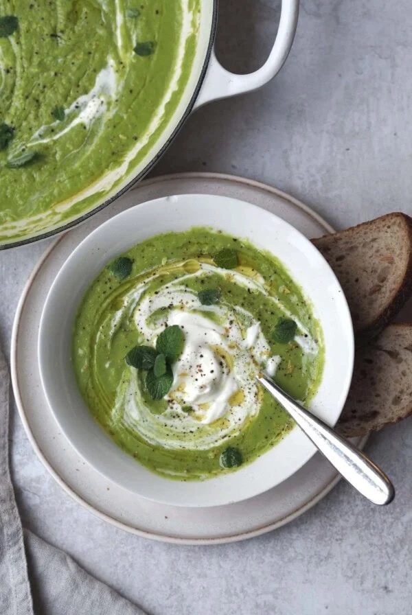 little gem, pea, mint soup in a white bowl with a pan of soup next to it