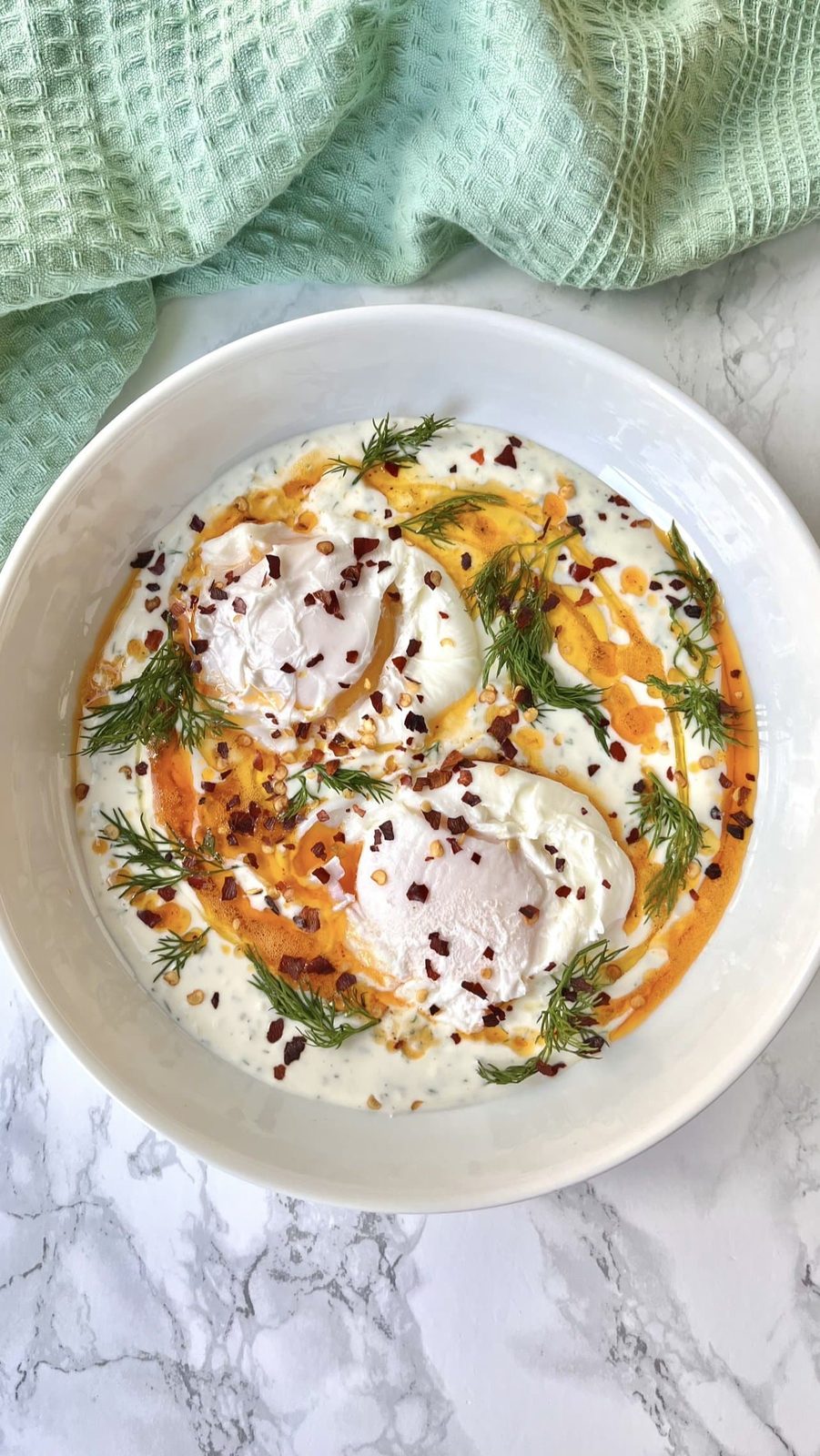 Turkish eggs with paprika butter and fresh dill in bowl near green napkin.