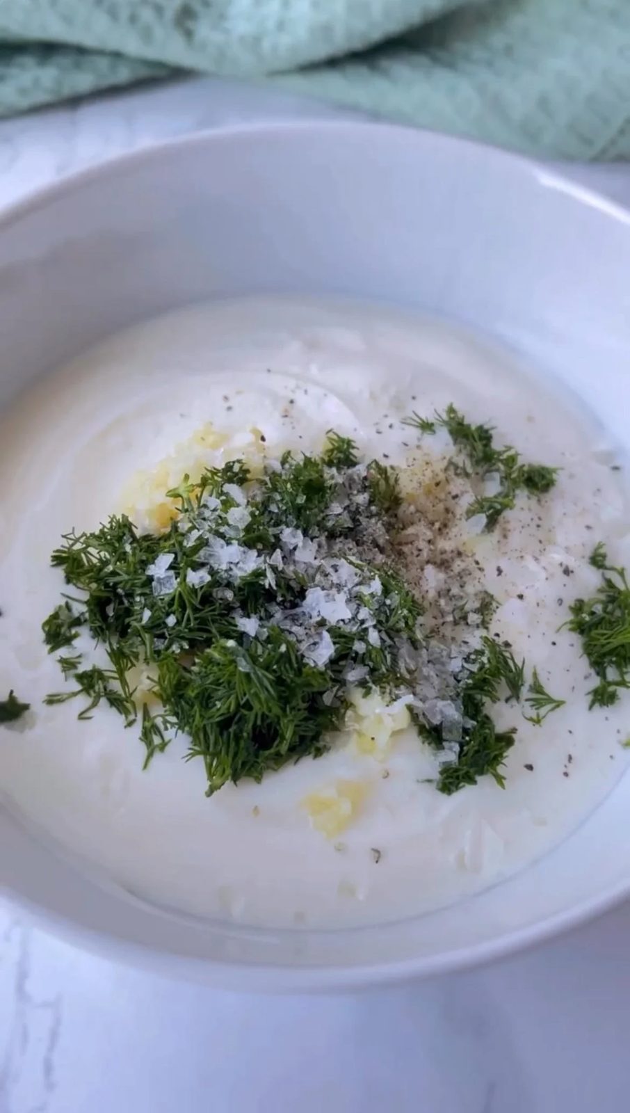 Mixing yogurt with garlic and dill in bowl.