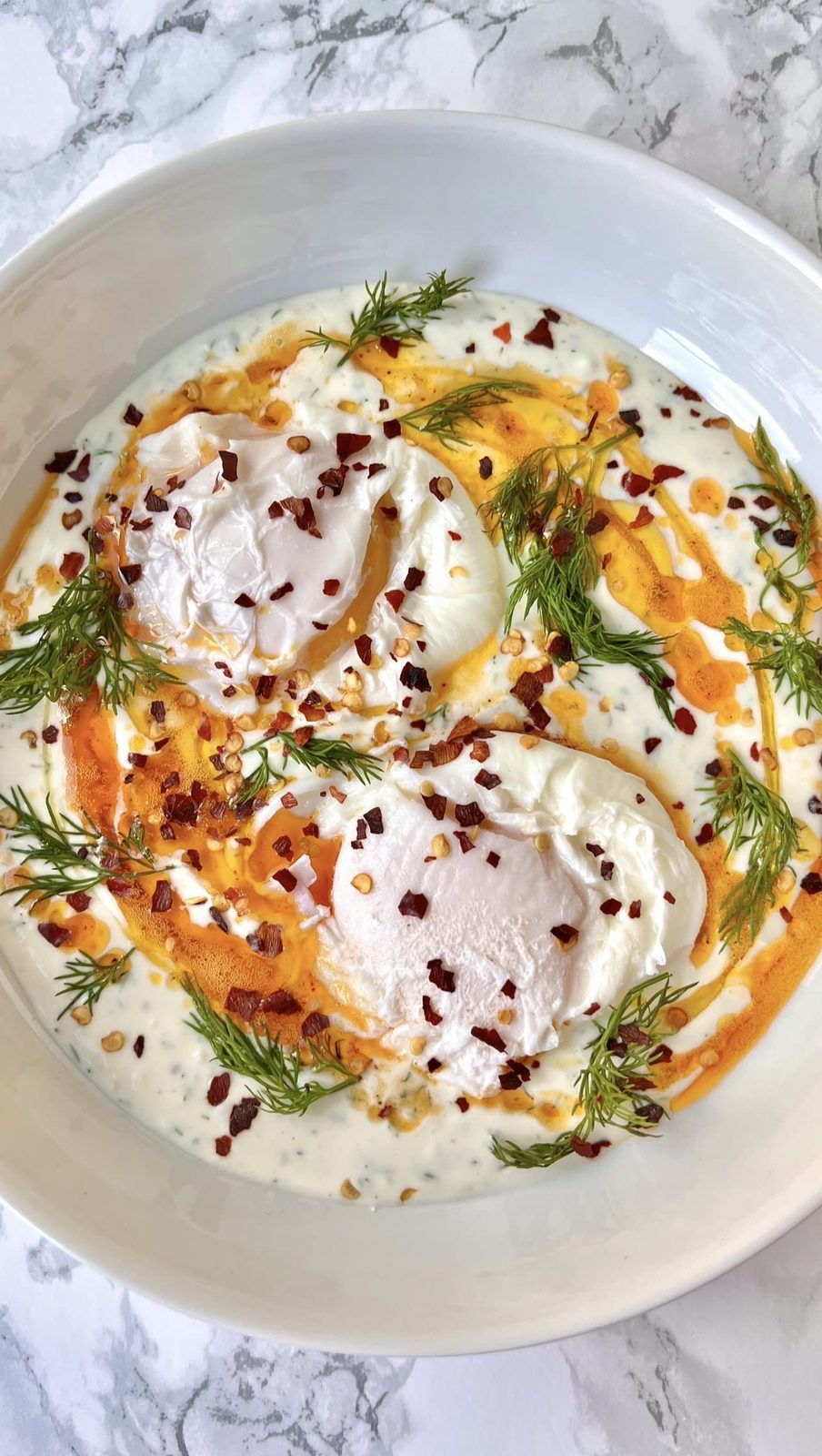 Turkish eggs on plate with fresh dill.