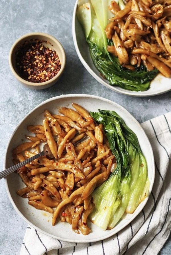 Two plates of scissor cut noodles in chilli oil with pak choi on the side.