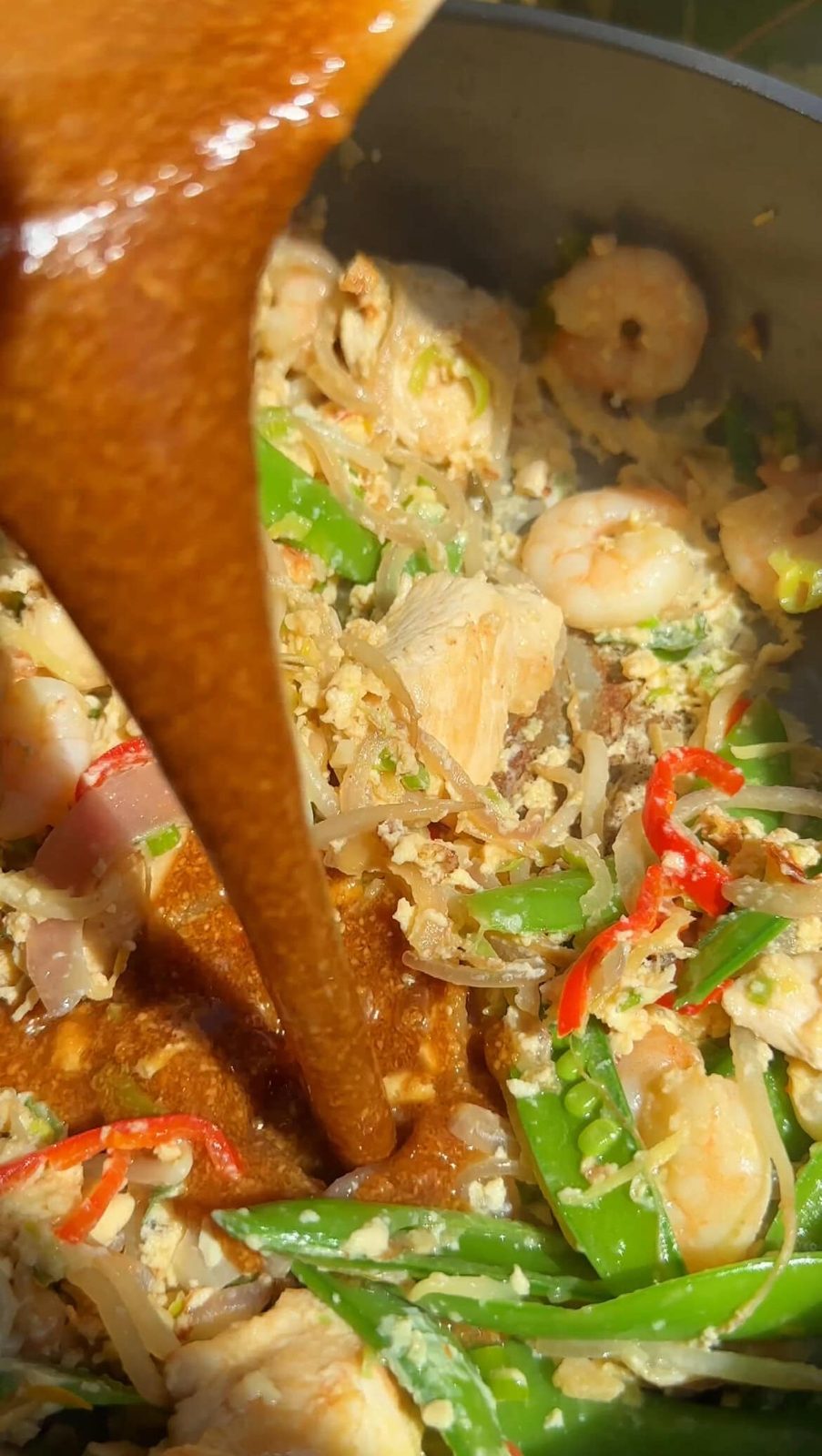 Adding Pad Thai sauce to chicken and vegetable stir-fry.