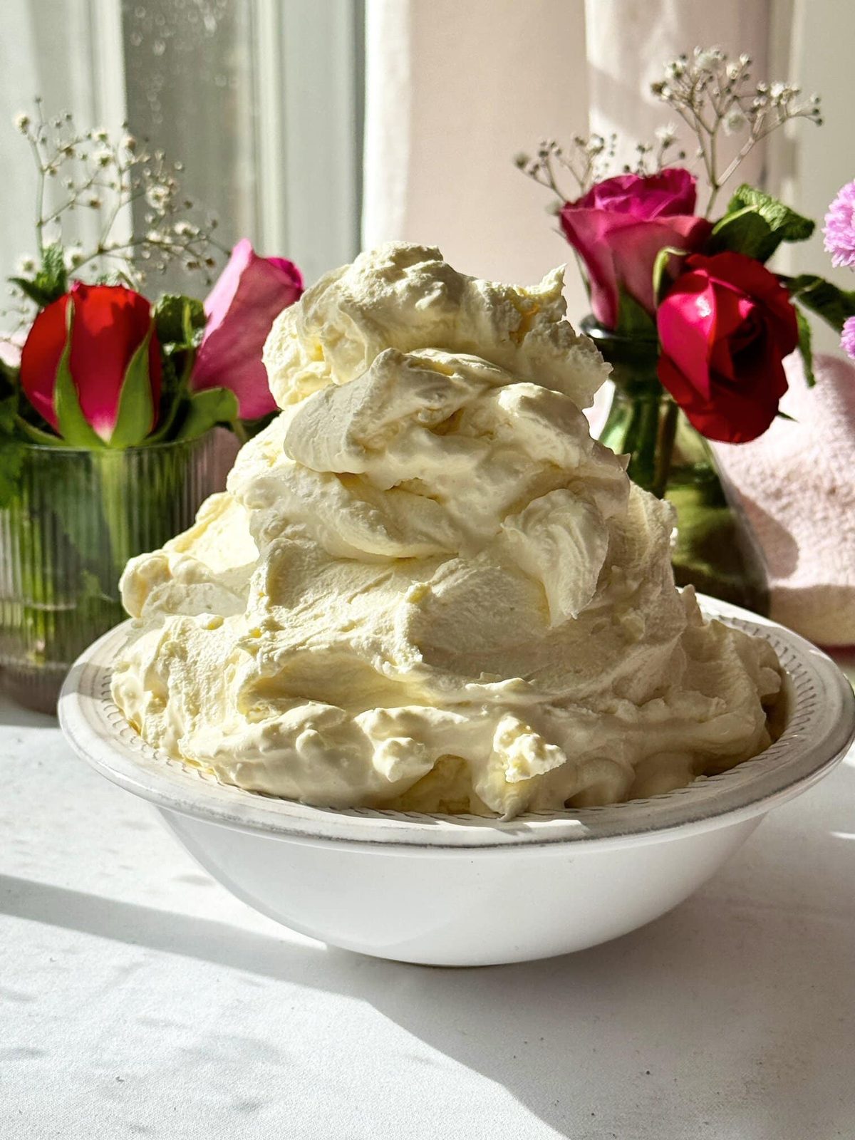 Whipped mascarpone cream in bowl on table with flowers.
