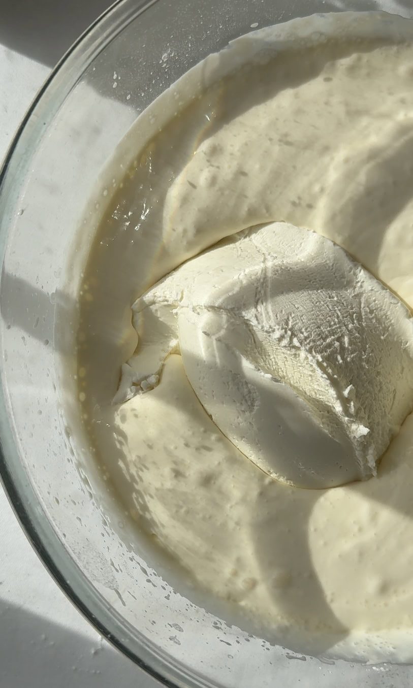 Adding mascarpone to whipped cream in bowl.