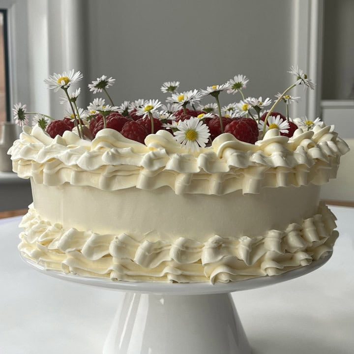 white chocolate raspberry cake on a white cake stand.