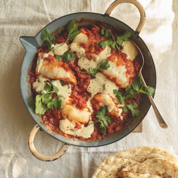 A pan of tomato sauce with white fish, tahini drizzle and coriander leaves scattered