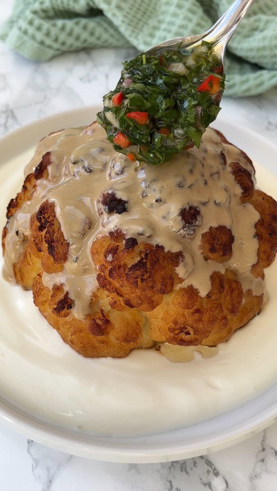 adding chimichurri to the tahini roasted cauliflower.