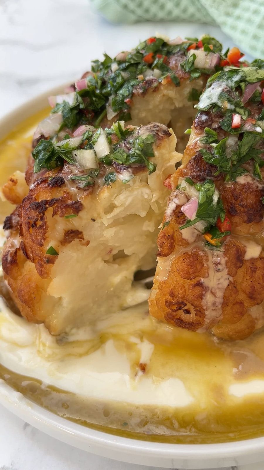 roasted cauliflower with tahini on a plate with slice removed.