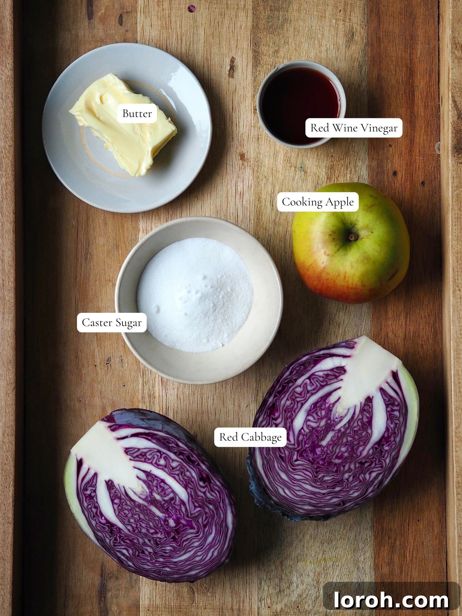 A selection of fresh ingredients, including red cabbage, apple, butter, nutmeg, sugar, and red wine vinegar, neatly arranged for making sticky red cabbage.