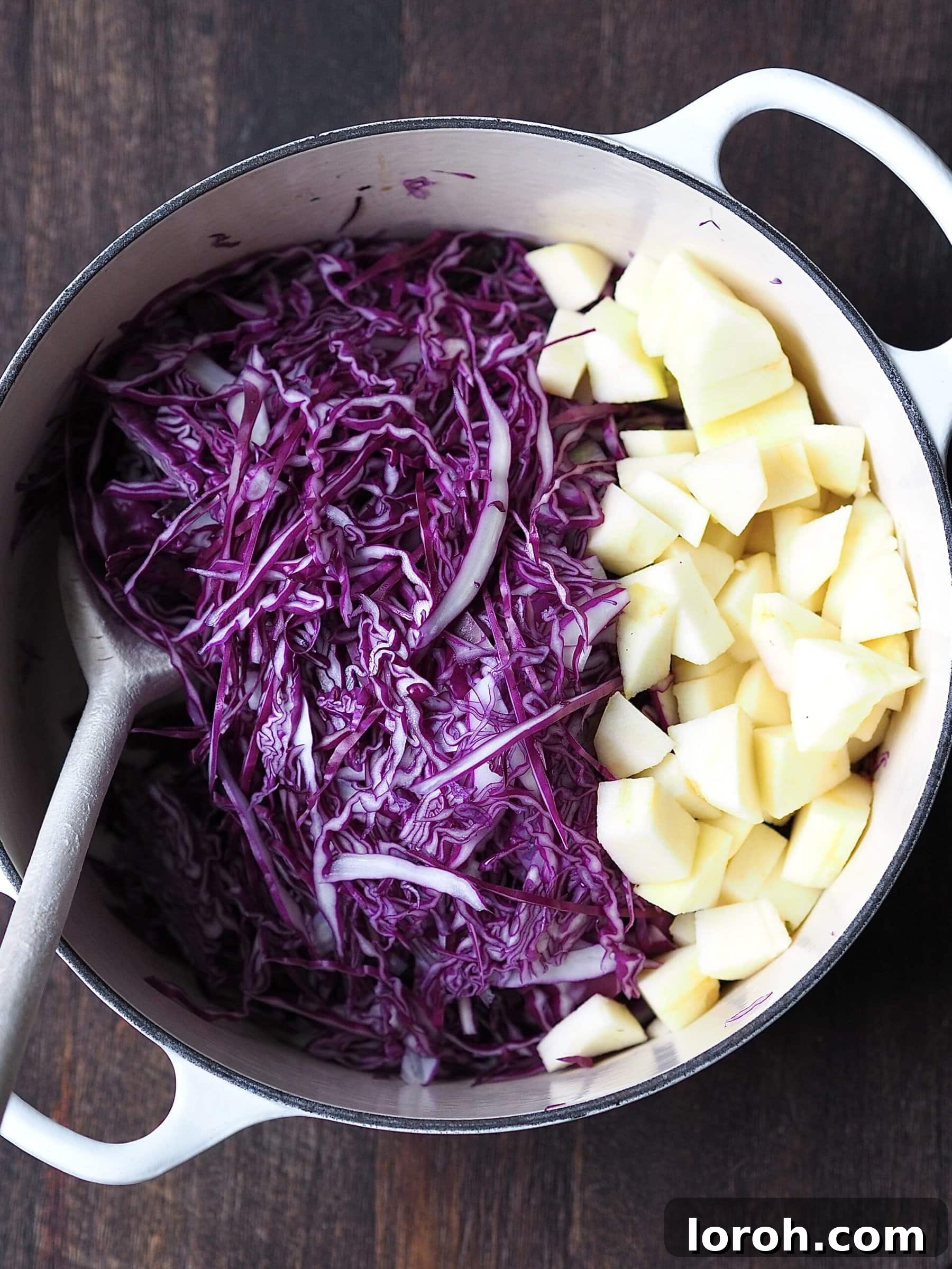 Shredded red cabbage and diced apple resting in a white casserole pot, ready for cooking.