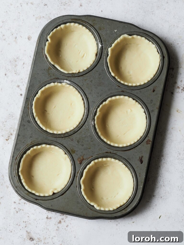 Muffin tin lined with shortcrust pastry circles, ready for filling.